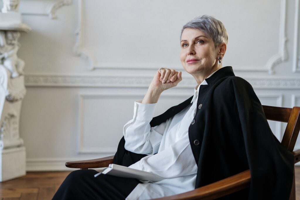 Senior woman with short hair seated indoors, exuding confidence and elegance in a classic setting.
